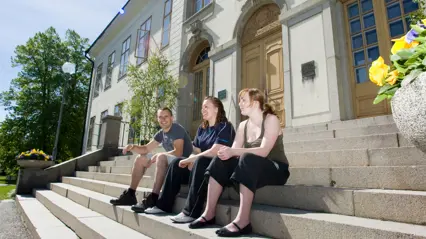 Three young people are sitting on a staircase to a mansion-like building. Photo: Jenny Svennås-Gillner