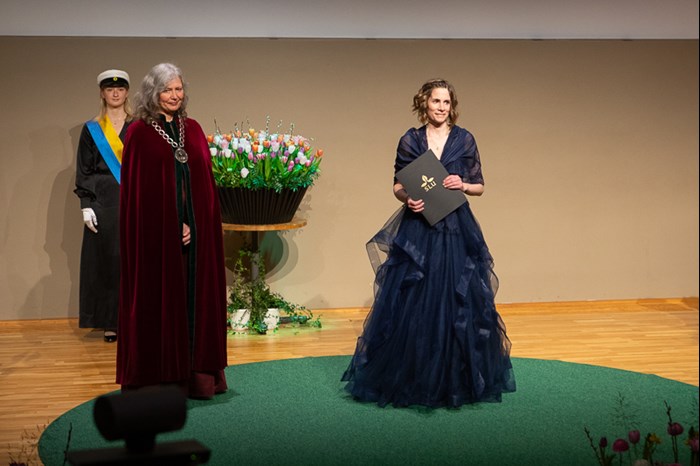 Professor Helena Nordh står högtidsklädd på scenen med sitt diplom. Till vänster i bilden står rektor. 