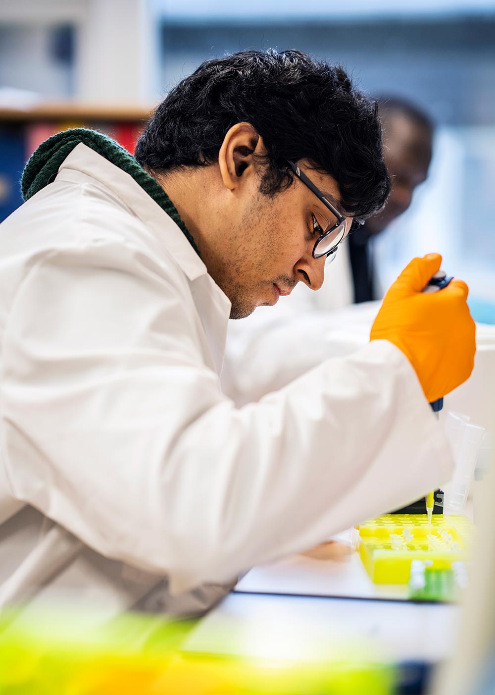 Picture of a person wearing a white coat in a laboratory, performing some sort of lab work while looking very concentrated.