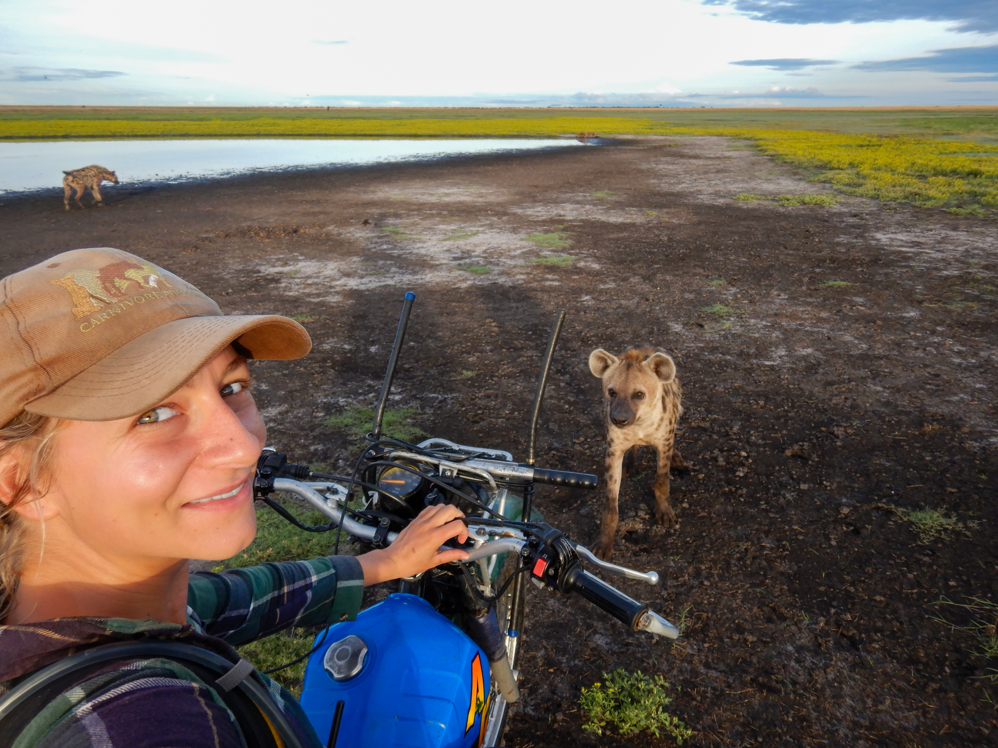 Selfie of Sandra on a motorbike with two hyenas nearby.