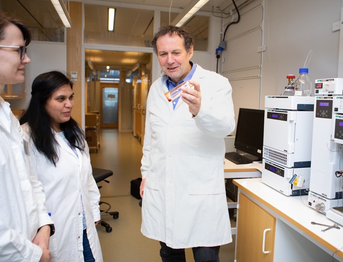 Picture of professor Volkmar Passoth in a conversation with his colleagues Johanna Blomqvist and Yashaswini Nagavara Nagaraj in the laboratory. Volkmar Passoth is holding a tube containing a red liquid.