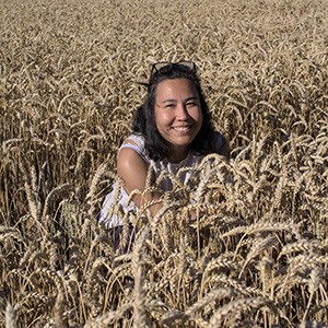 Woman with long dark hair kneeling in field of wheat