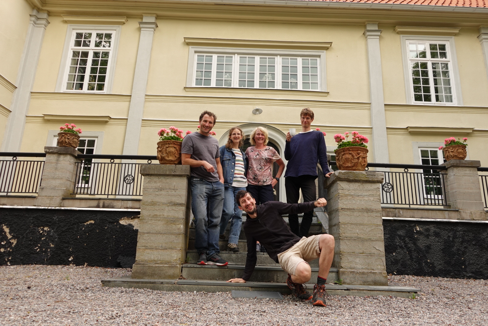 five people posing at a staircase in front of a mansion