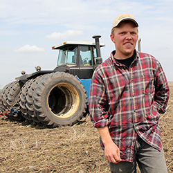 A young man in a cap standing in front of a large tractor. Photo.