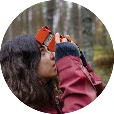 A woman looks through an orange device at forest. Photo.