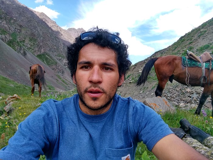 Raul in mountain, horses in the background. Photo.