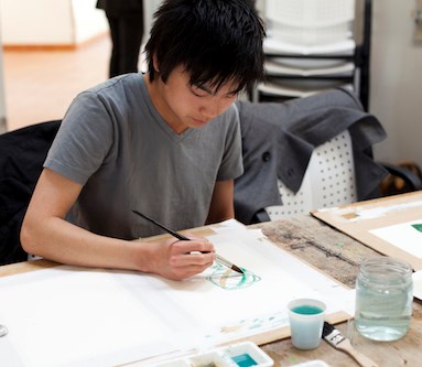 Ung person målar med vattenfärg, sittandes vid ett bord
