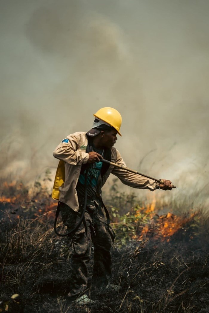 A man in a yellow helmet puts out a grass fire.