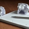 Ett anteckningsblock, två ihopskrynklade pappersark och en penna på ett bord. 