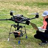 Woman sitting next to big drone on lawn. Photo.