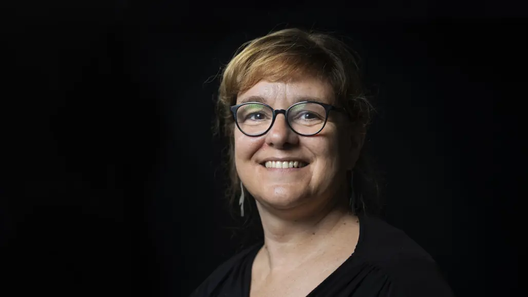 Porträtt av Stéphanie Robert iklädd svart klänning mot svart bakgrund. Hon har glasögon och brunt hår.