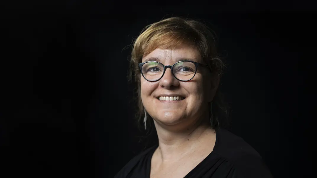 Portrait of Stéphanie Robert wearing a black dress in front of a black background. She has glasses and brown hair.