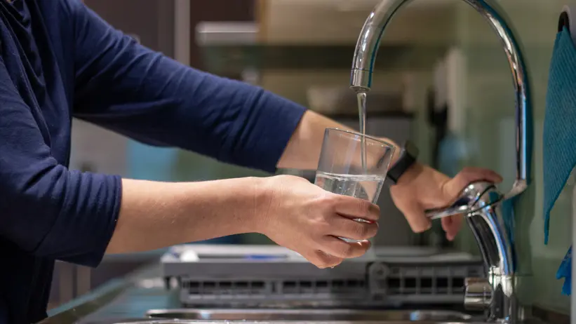Photo of a person filling a glass of water from a tap indoors in a kitchen.