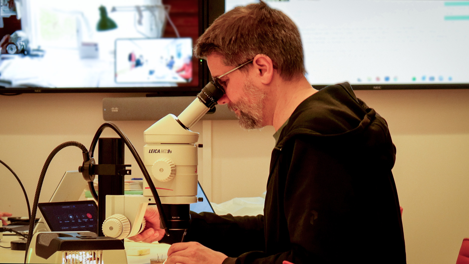 Man i mötesrum tittar i mikroskop. Foto