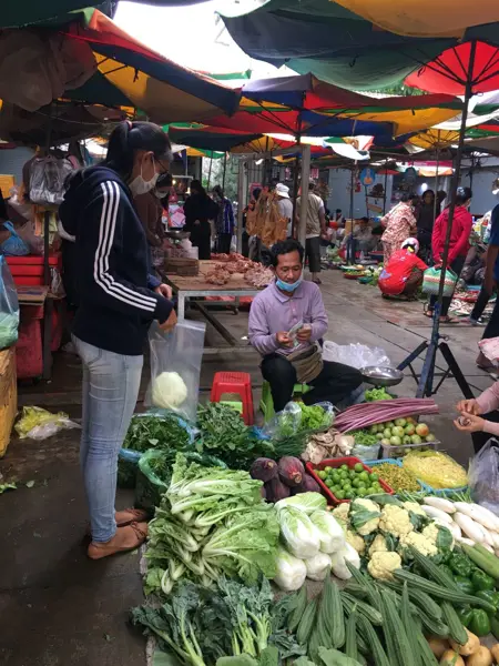 Market vendors and customers at a vegetable stand at a market in Cambodia. Photo.