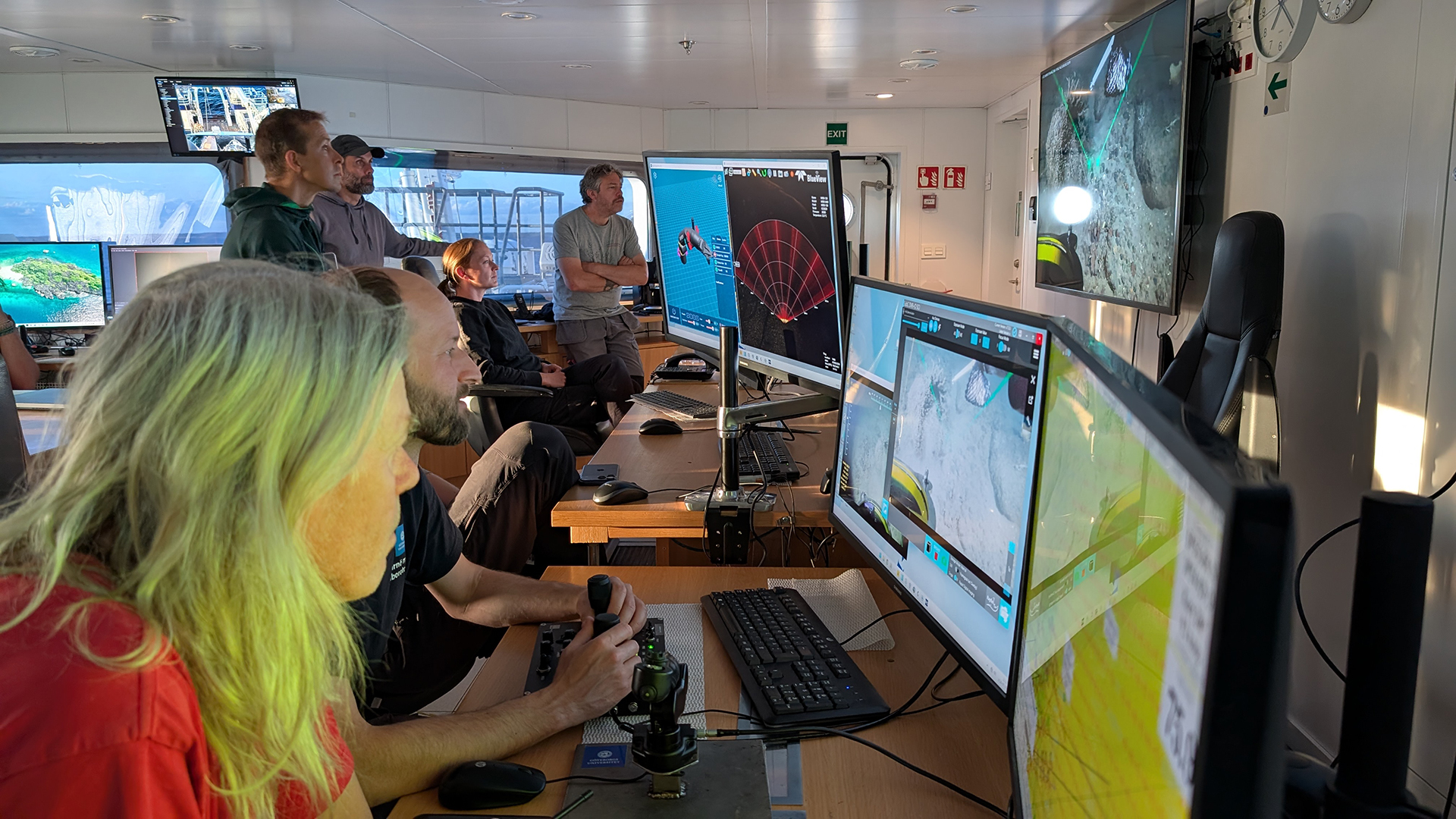 Persons in front of multiple screens.