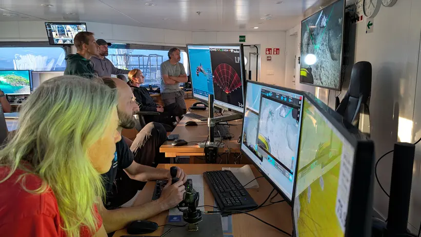 Persons in front of multiple screens.