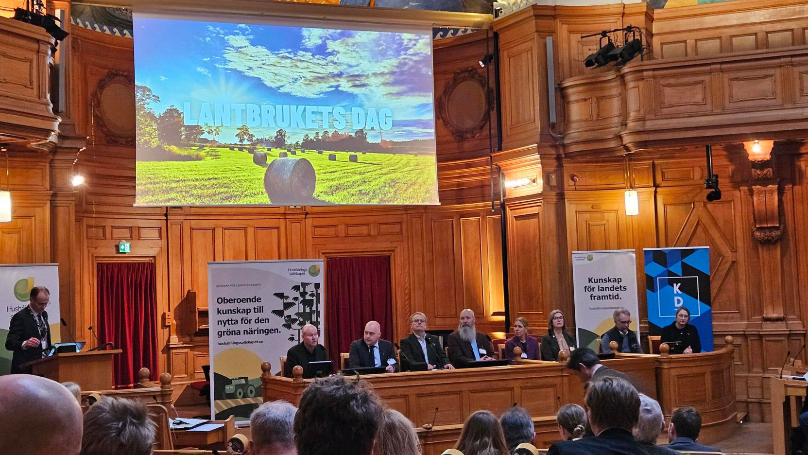 Åtta personer sitter på rad i högtidlig miljö