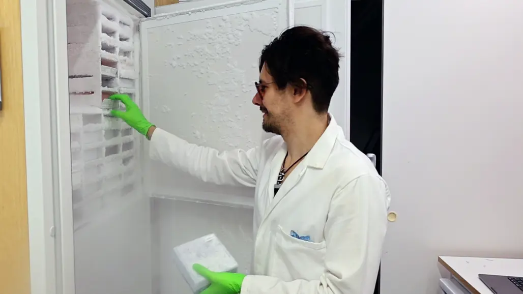 Lab worker standing by an open freezer with samples. Photo.