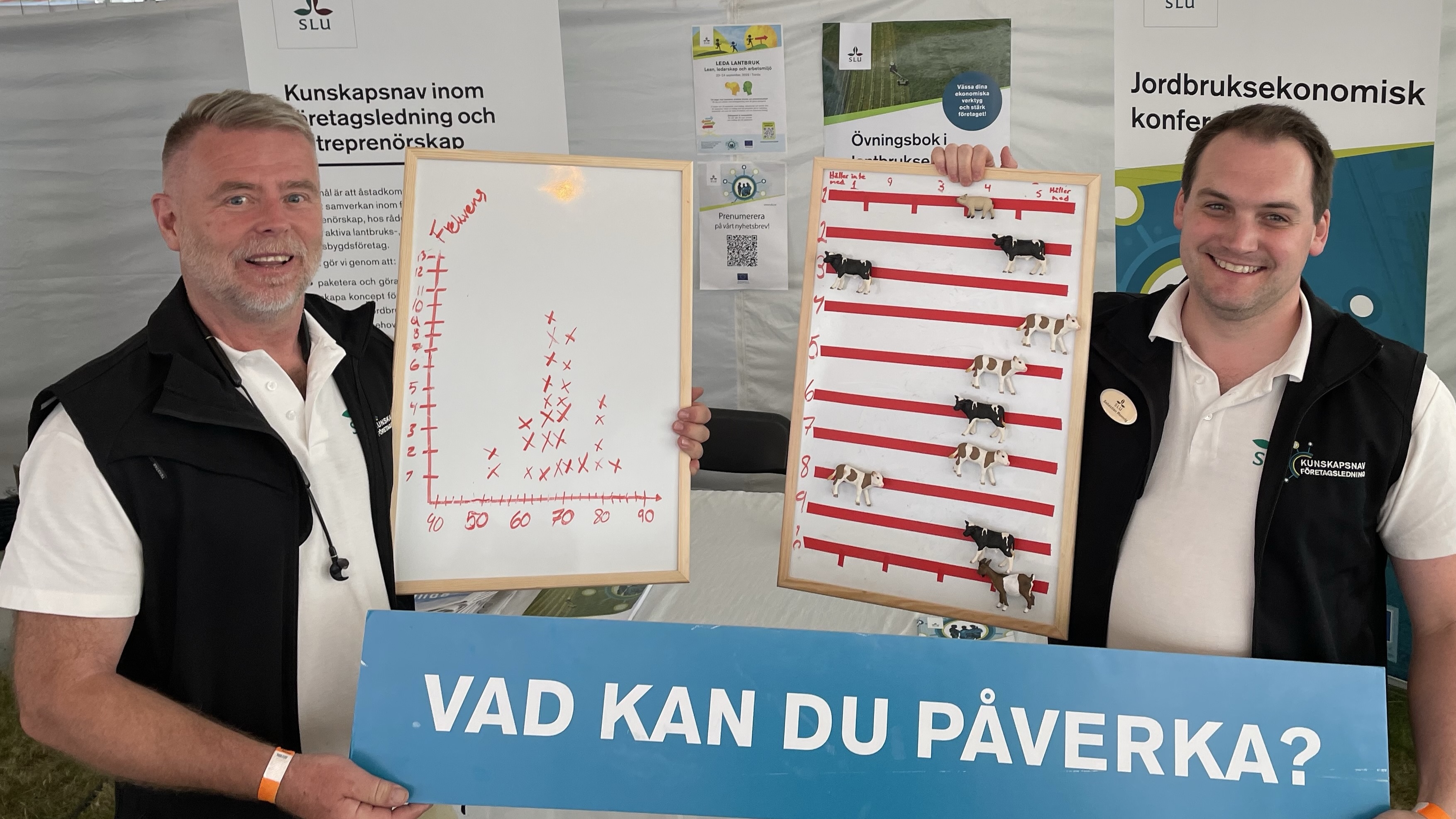 Två män visar upp en vi tavla med plastkor