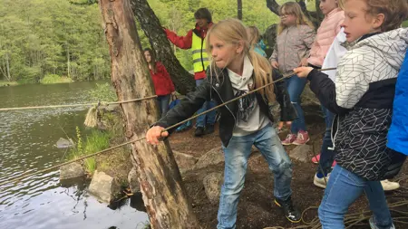 En grupp barn står vid vattnet och drar i ett rep.