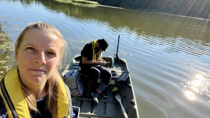 Two people in a small boat on a sunlit lake, both wearing yellow life jackets.