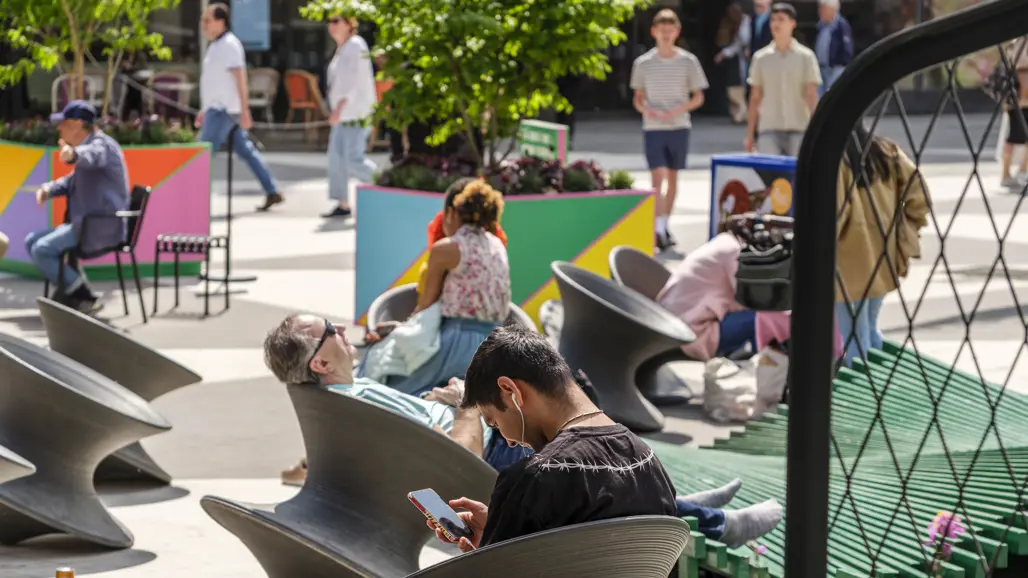 Folk som sitter ner på Sergels torg, några tar det lugnt för sig själva och andra konverserar.