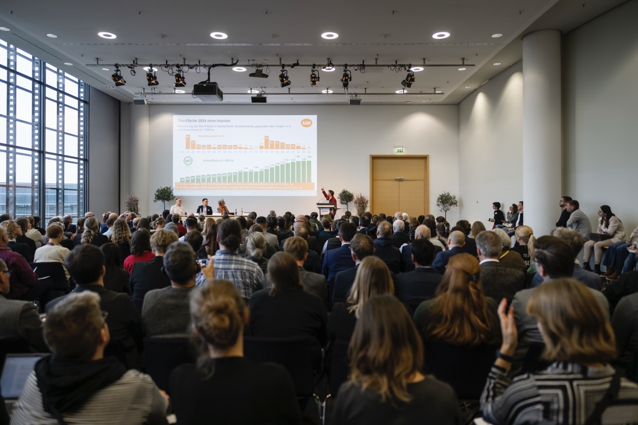 Foto från kongressen på Biofach, en person föreläser inför en stor publik, grafer projiceras i bakgrunden.