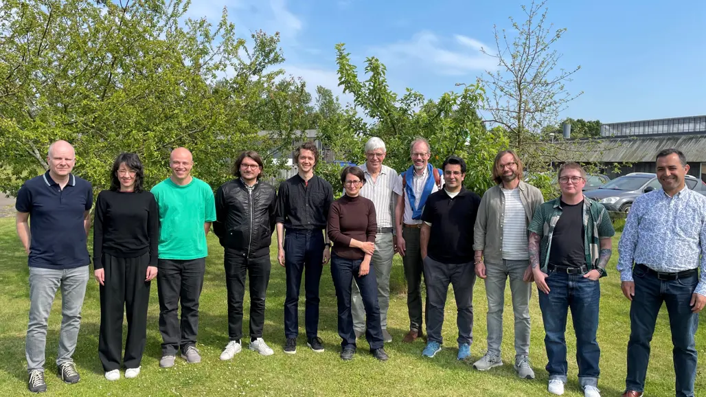 Twelve people are standing on a lawn in the sun