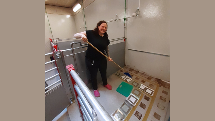 Woman dressed in black standing holding a broom, standing inside a small enclosure.