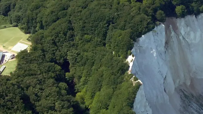 Bilden visar en byggnad till vänster och en massiv vit bergvägg till höger. Framför ligger havet.