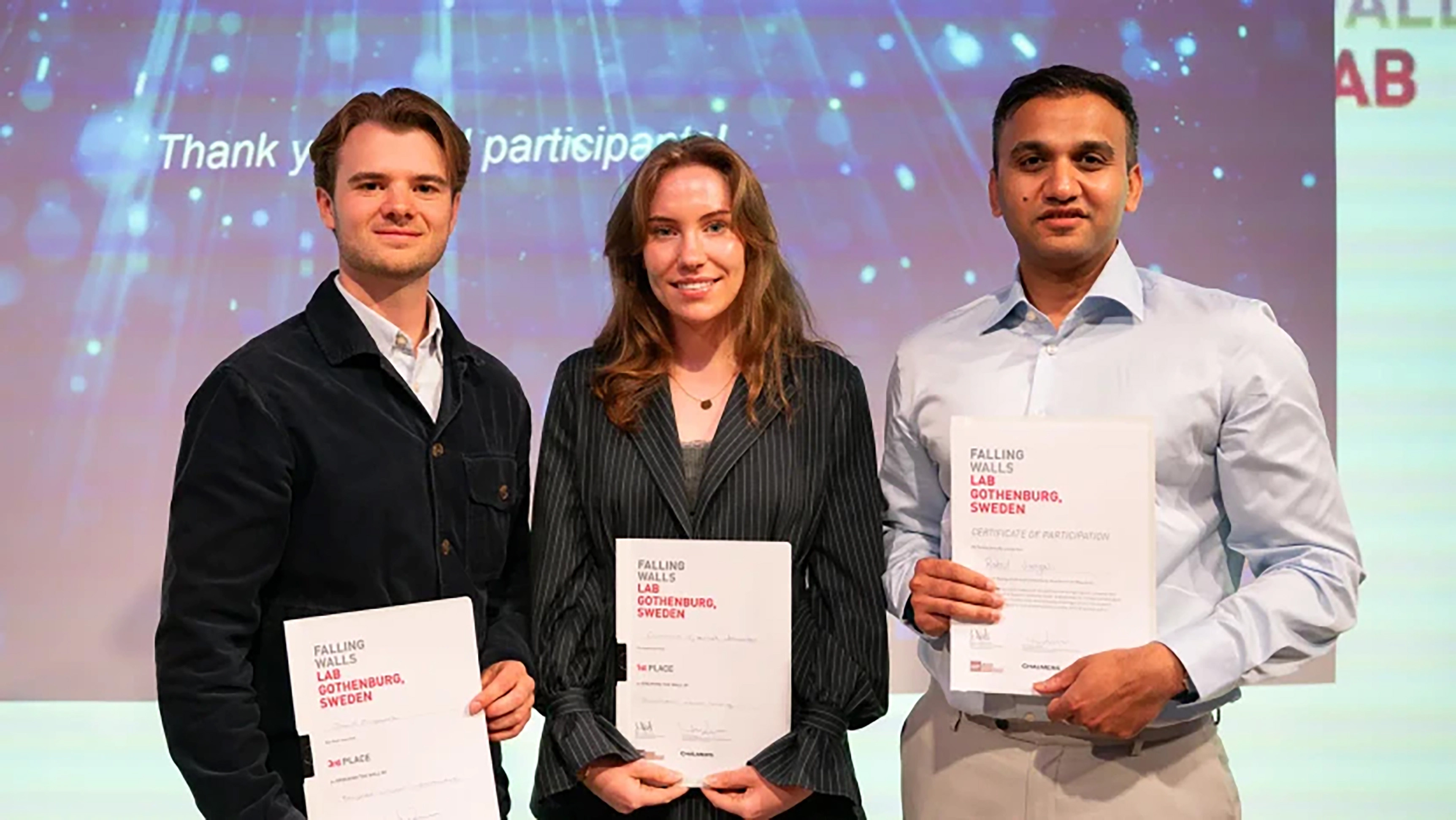 Tre persons standing together, each holding a certificate in their hands: a woman in the middle and a man on both sides of her.  