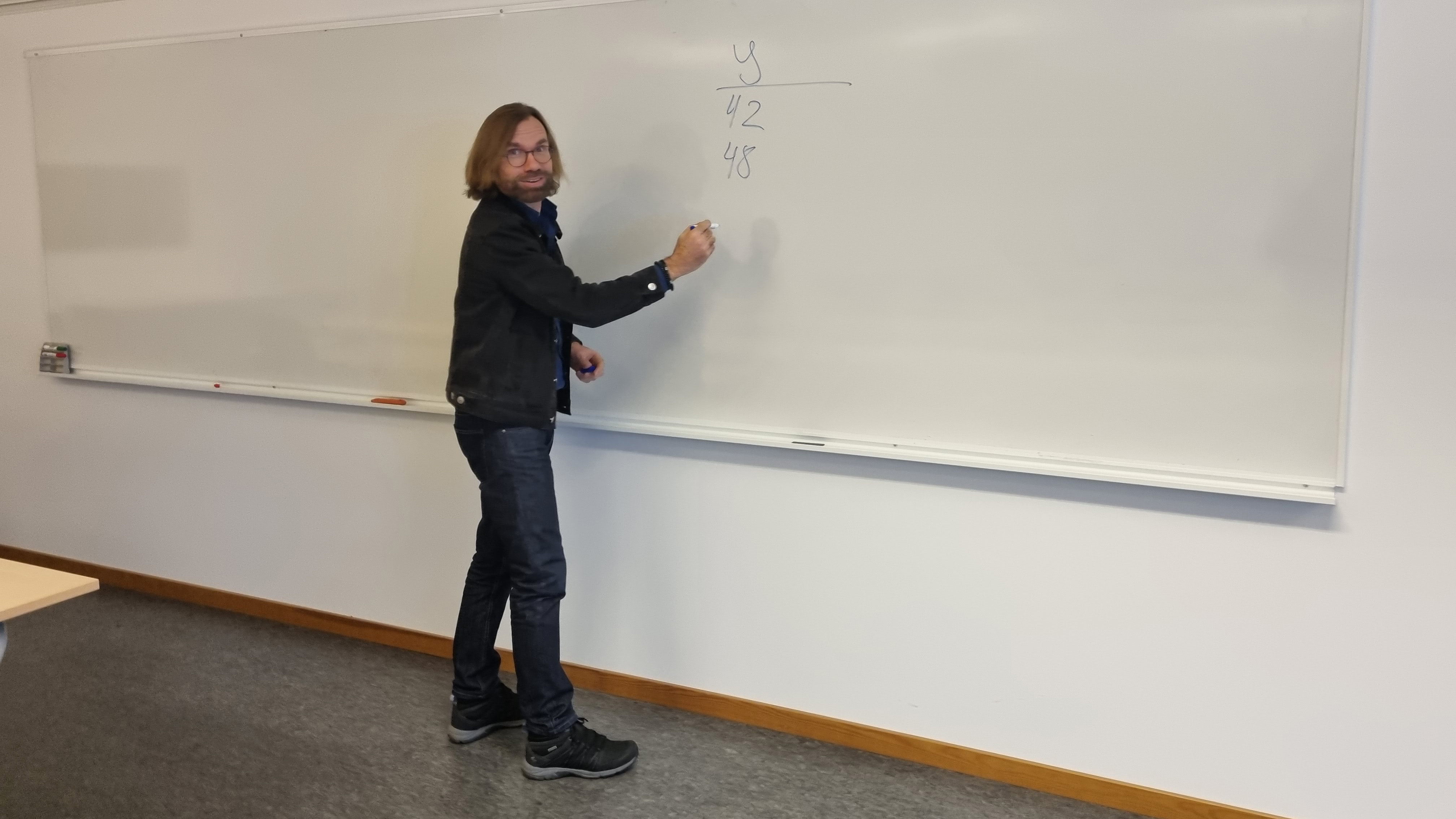 En man skriver siffror på en whiteboard-tavla.