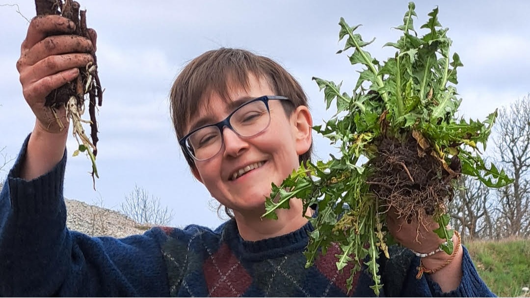 Person outdoors smiling while holding up freshly pulled plants with roots.