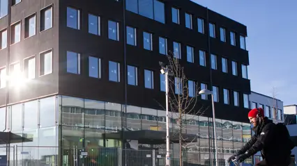 Modern byggnad med svart fasad och glaspartier, Ulls hus på SLU:s campus i Uppsala, vintertid med snö på marken och en cyklist med röd mössa i förgrunden.