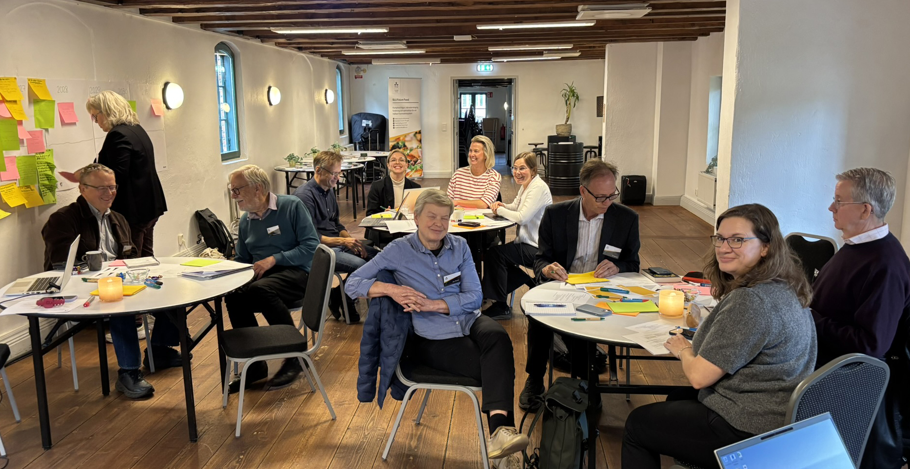 Elva glada personer sitter runt tre runda bord. Foto.