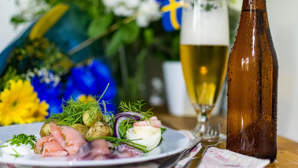En silltallrik med en svensk flagga i bakgrunden och en ölflaska. Foto.