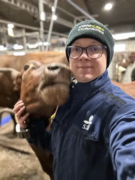 A portrait of a person with a cow in a barn.