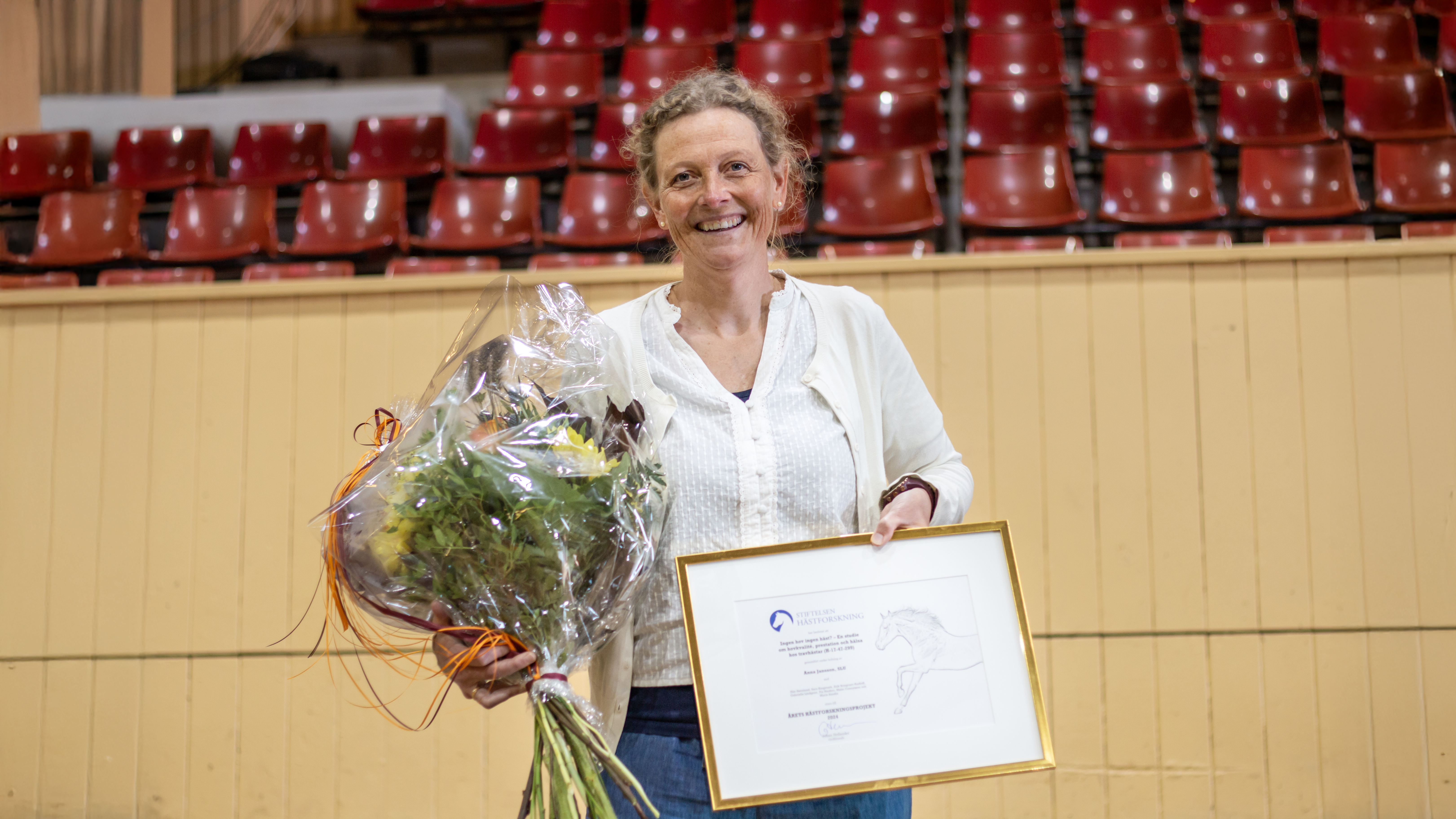 Foto av en kvinna (Malin Connysson, SLU) som tar emot pris i ett ridhus.