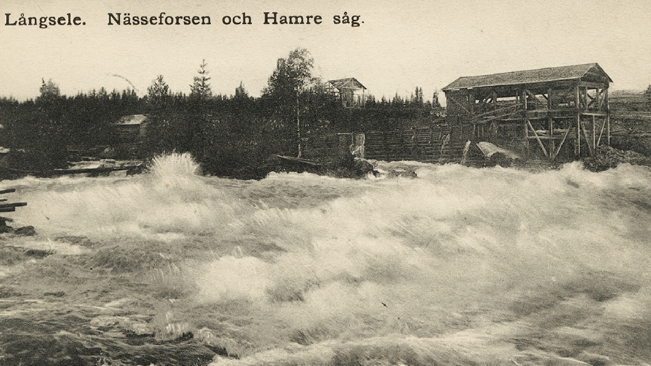Svart-vit fotografi över en fors med byggnader i bakgrunden.