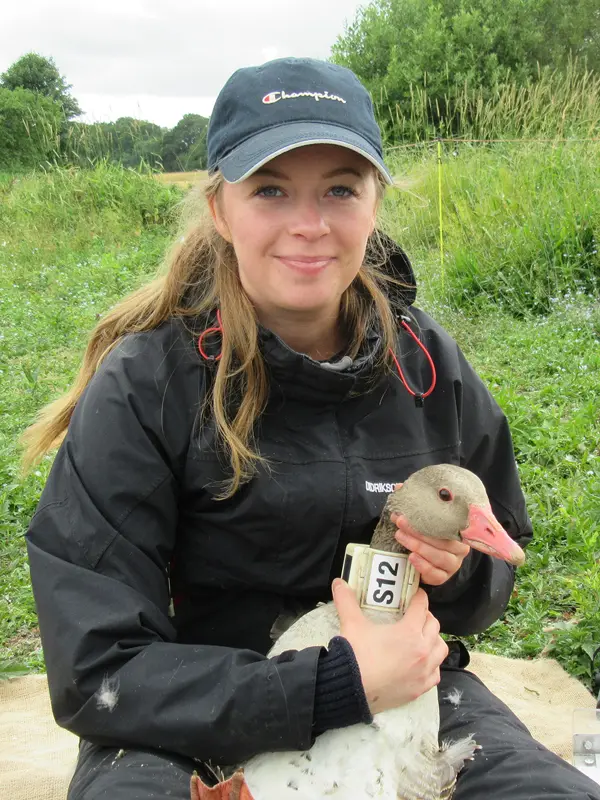 En kvinna sitter med en märkt gås i famnen.