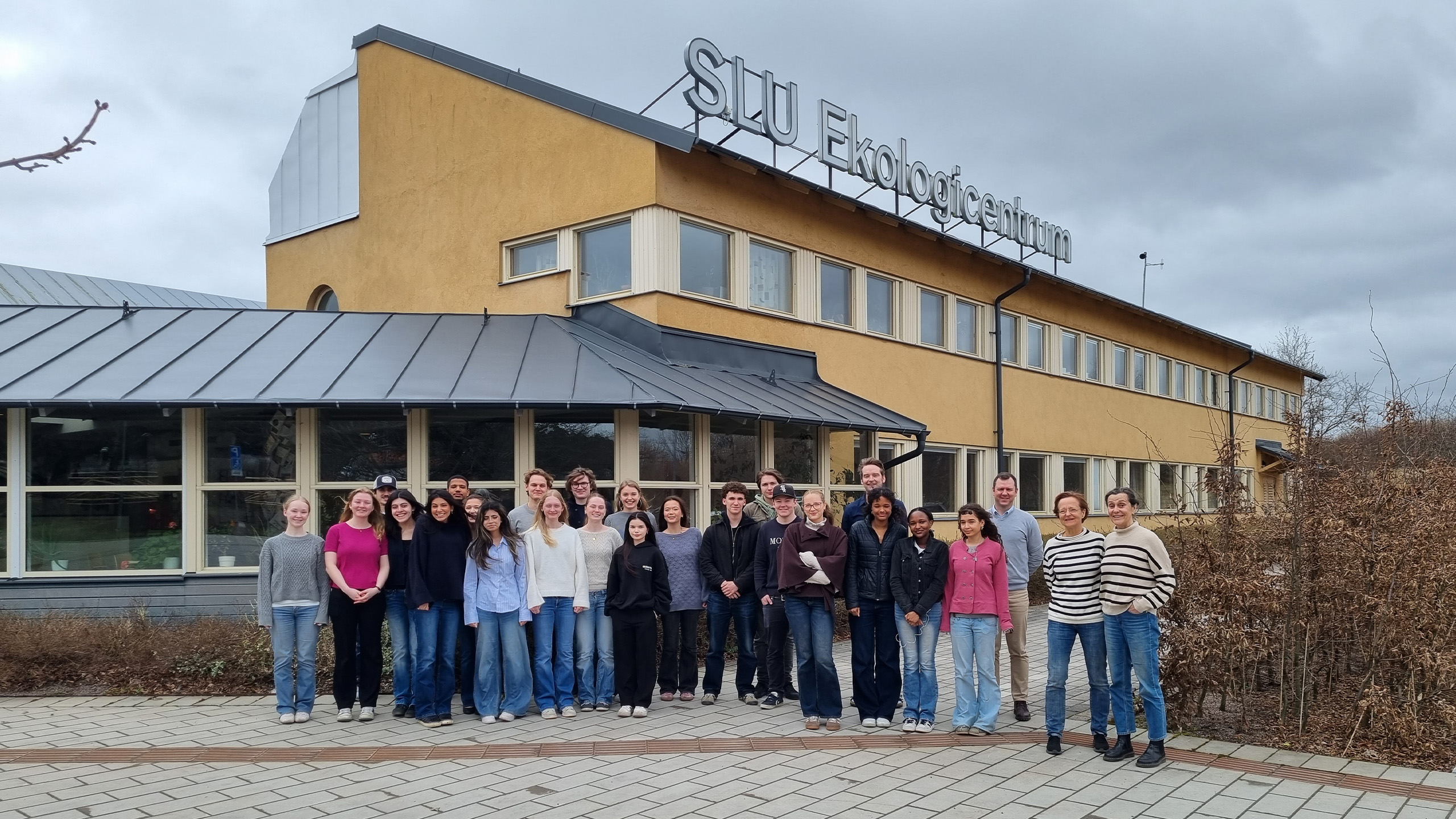 26 personer står framför en gul byggnad med en skylt på taket med texten Ekologicentrum.