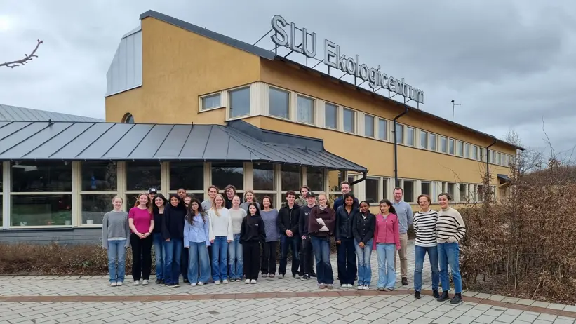 26 personer står framför en gul byggnad med en skylt på taket med texten Ekologicentrum.