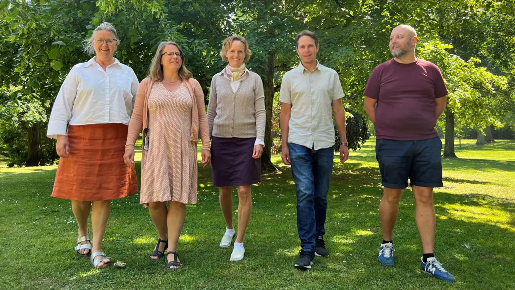 Tre kvinnor och två män i en grön omgivning