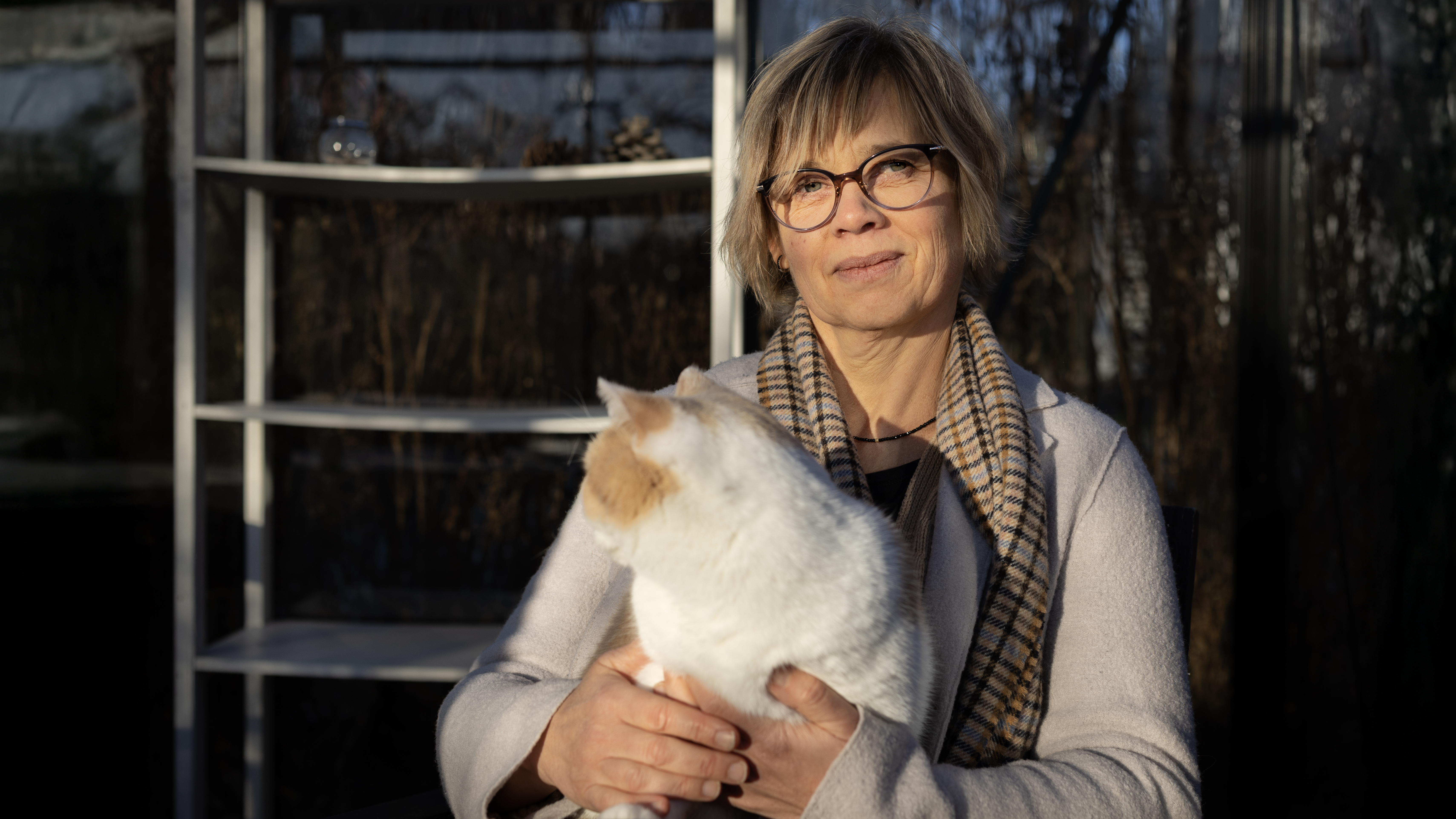 Photo of a woman (Cecilia Ley) sitting outdoors in the sun with a cat on her lap.