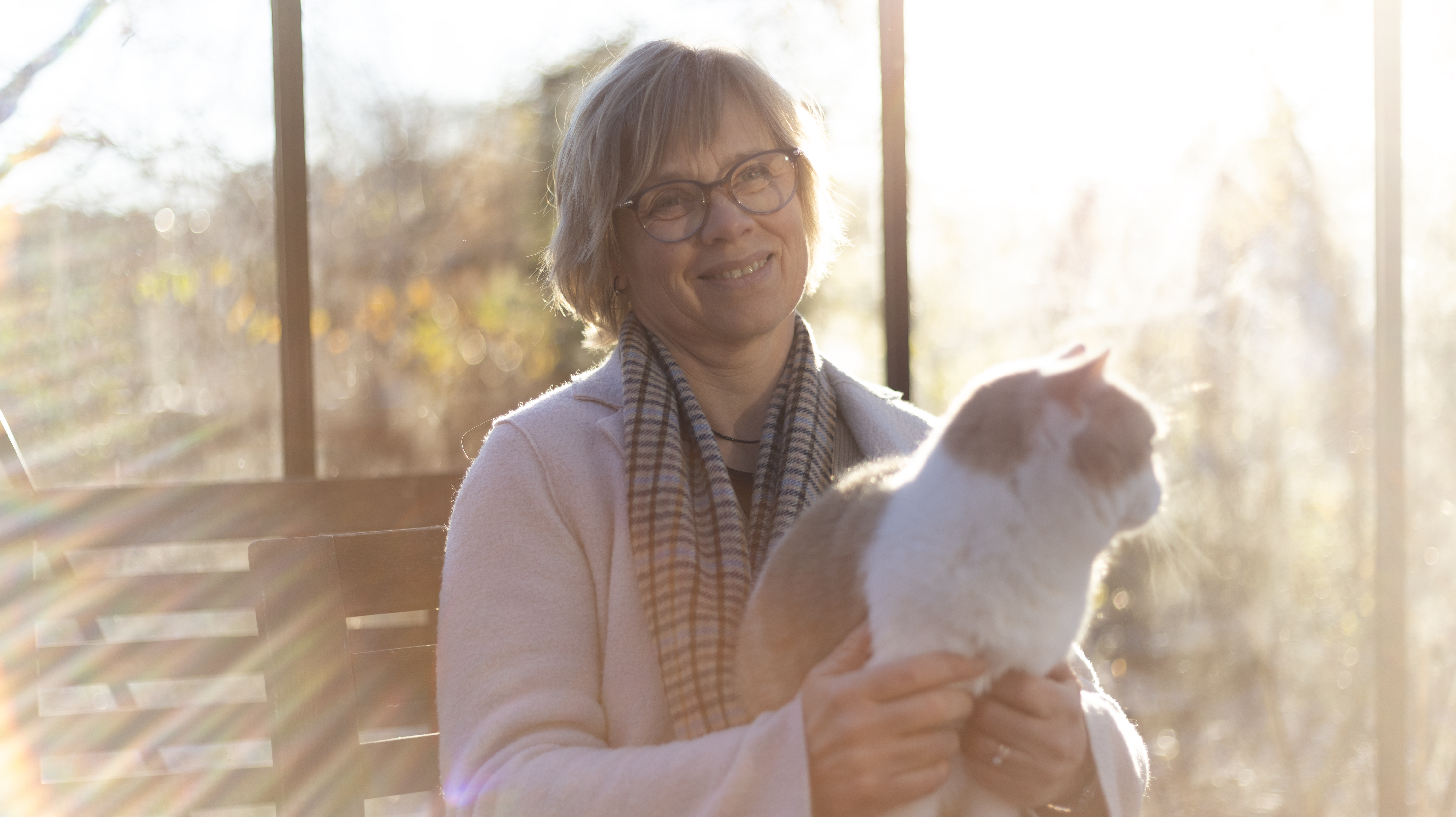 Foto av en kvinna (Cecilia Ley, SLU) sittandes med en katt i knät i motljus.