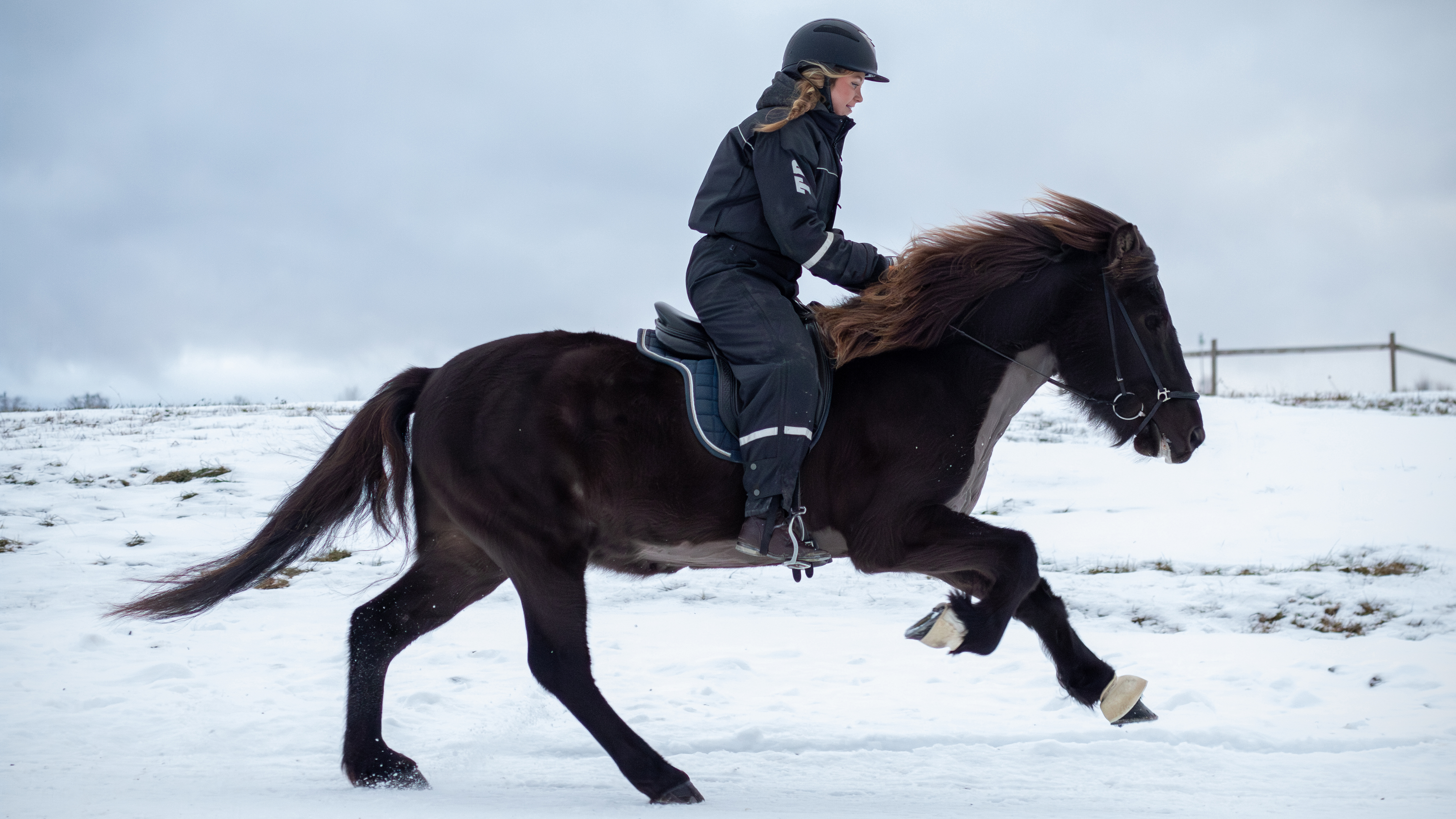 Foto av en kvinna som galopperar snabbt med en islandshäst utomhus på snö under vinter.