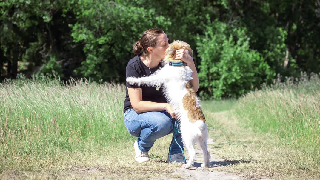 A woman cuddles with a dog on a walking path. Photo.