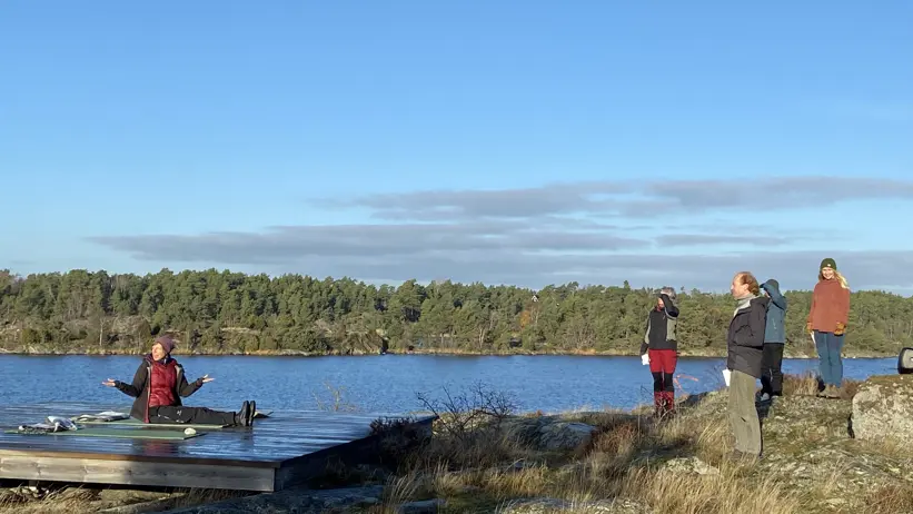 Fyra personer tittar på en person som sitter på en plattform vid vatten