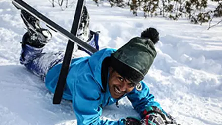 En man med skidor, som ligger i snön. Foto.